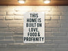 a sign that says this home is built on love, food and profanity