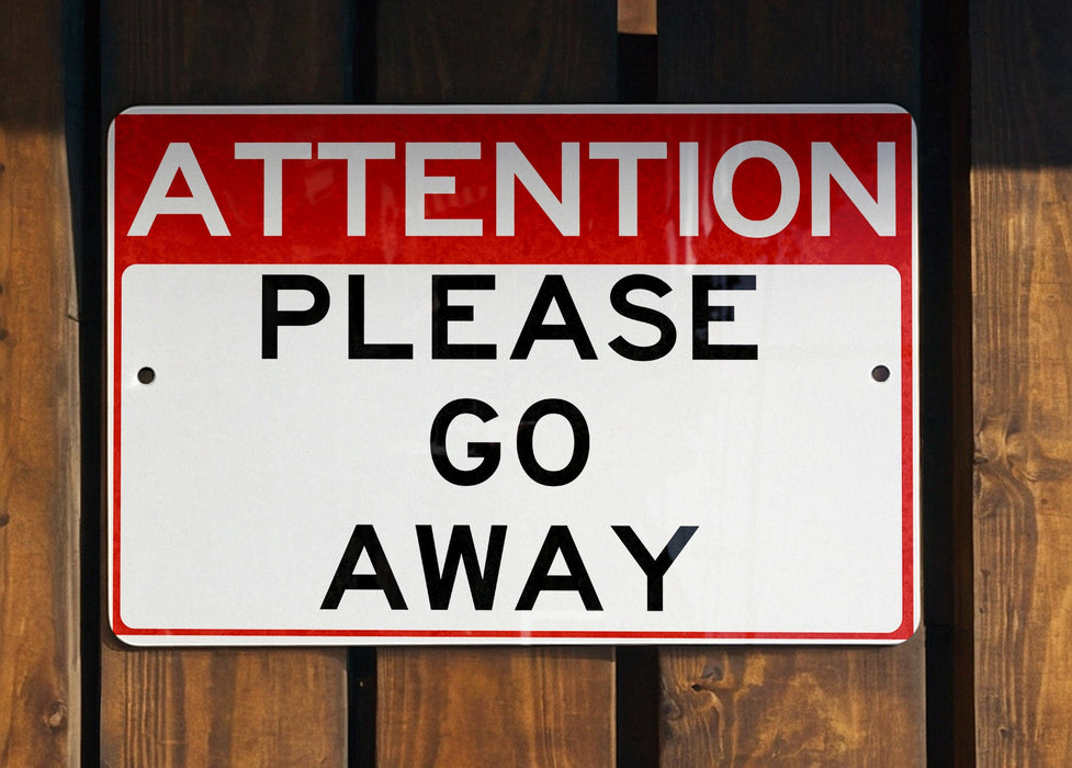 a red and white street sign hanging from the side of a wooden fence