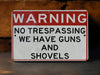 a red and white warning sign stating no trespassing we have guns and shovel