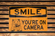 a yellow sign that says smile you're on camera