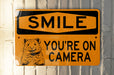 a yellow sign that says smile you're on camera