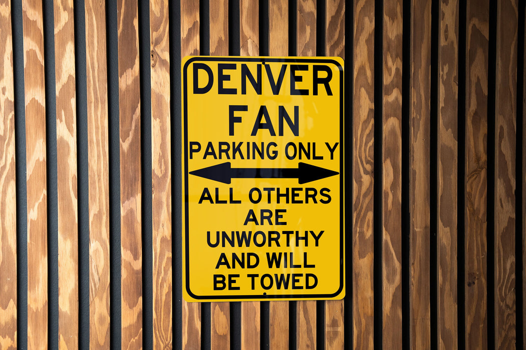 a yellow sign on a wooden fence that says denver fan parking only all others are