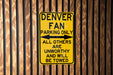 a yellow sign on a wooden fence that says denver fan parking only all others are