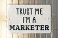 a white sign that says trust me i'm a marketer