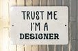 a white sign that says trust me i'm a designer