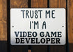 a white sign that says trust me i'm a video game developer