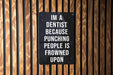 a sign on a wooden wall that says i'm a dentist because punching people