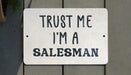 a white sign that says trust me i'm a salesman