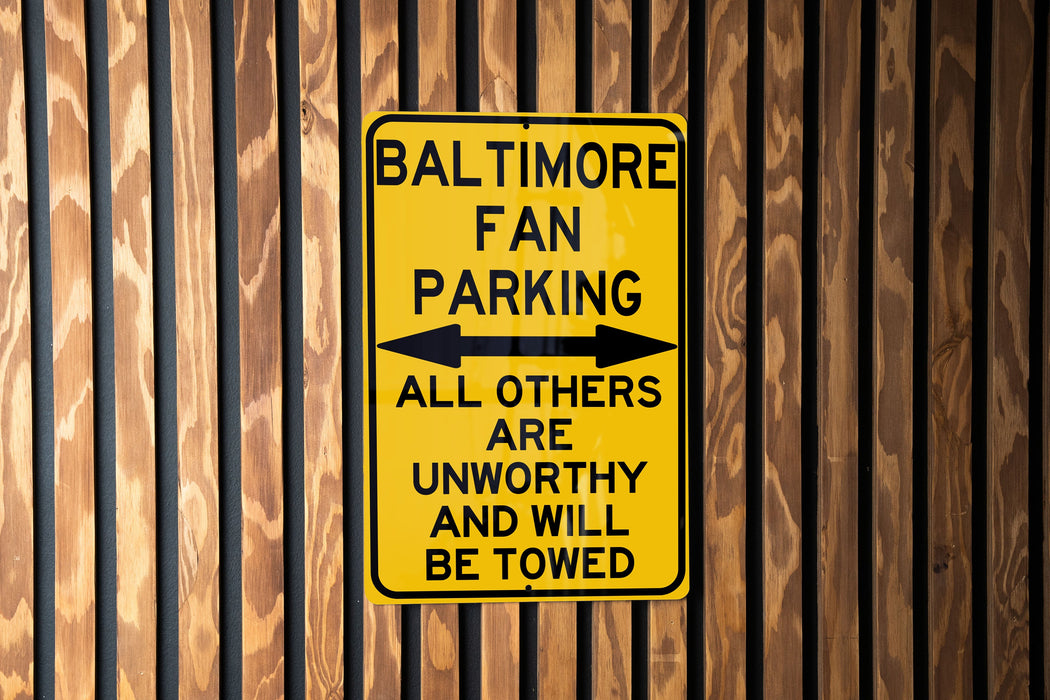 a yellow sign on a wooden fence that says baltimore fan parking all others are un