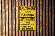 a yellow sign on a wooden fence that says baltimore fan parking all others are un