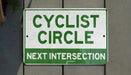 a green and white sign that says cyclist circle next intersection