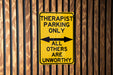 a yellow sign on a wooden fence that says, therapist parking only