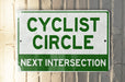 a green and white sign that says cyclist circle next intersection
