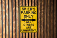 a yellow sign on a wooden fence that says skier's parking only all others
