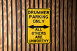 a yellow sign on a wooden fence that says drummer parking only all others are un