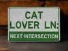 a green and white sign that says cat lover ln next intersection
