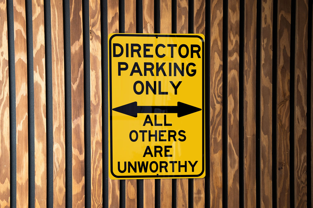 a yellow sign on a wooden fence that says director parking only all others are un