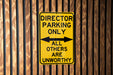 a yellow sign on a wooden fence that says director parking only all others are un