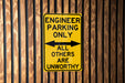 a yellow sign on a wooden fence that says engineer parking only all others are un