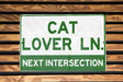 a green and white sign that says cat lover ln next intersection