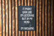 a sign on a wooden wall that says it might look like i'm listening