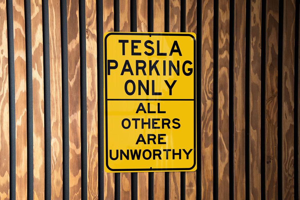 a yellow sign on a wooden fence that says tesla parking only all others are un