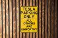 a yellow sign on a wooden fence that says tesla parking only all others are un