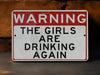 a red and white warning sign stating girls are drinking again