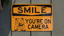 a yellow sign that says smile you're on camera