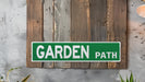 a green garden path sign mounted to a wooden wall
