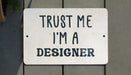 a white sign that says trust me i'm a designer