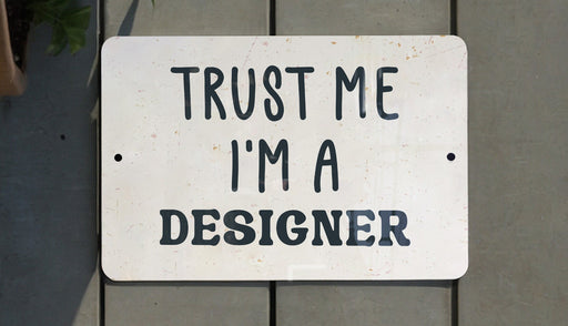 a white sign that says trust me i'm a designer