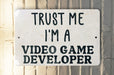 a white sign that says trust me i'm a video game developer