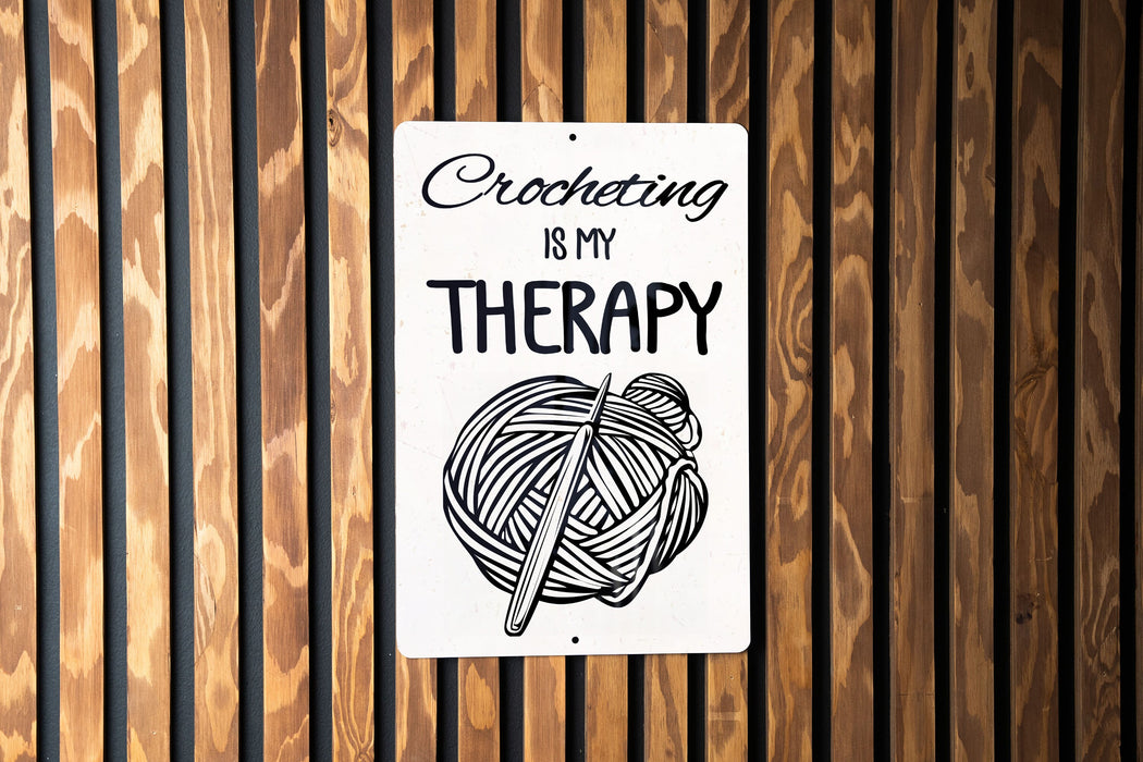 a sign on a wooden wall that says crocheting is my therapy