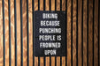 a sign on a wooden wall that says biking because punching people is frowned upon