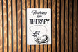 a sign on a wooden wall that says fishing is my therapy