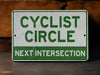 a green and white sign that says cyclist circle next intersection