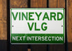 a green and white sign that says vineyard vlg next intersection