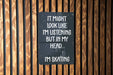 a sign on a wooden wall that says it might look like i'm listening