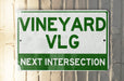 a green and white sign that says vineyard vlg next intersection