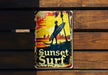 a tin sign that says sunset surf on a wooden wall