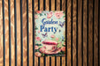 a garden party sign hanging on a wooden wall