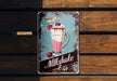 a metal sign on a wooden wall advertising milkshake bar