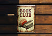 a book club sign hanging on a wooden wall