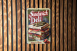 a sandwich deli sign hanging on a wooden wall