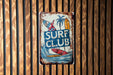a surf club sign hanging on a wooden wall