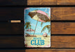 a beach club sign on a wooden bench