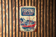 a fishing village sign hanging on a wooden wall