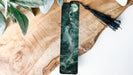 a green and black bookmark with a tassel on it