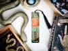 a bookmark with a snake and a book on top of it